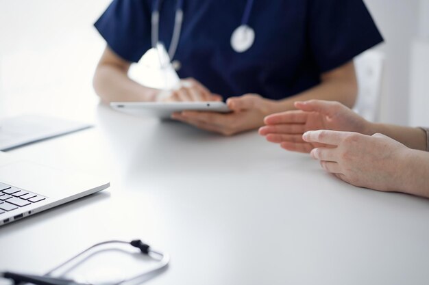 Médico e paciente conversando durante o exame de saúde atual enquanto estão sentados na mesa da clínica, close-up da mão. Serviço médico perfeito e conceito de medicina.