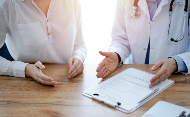 Médico e paciente discutindo algo enquanto estão sentados próximos um do outro na mesa de madeira da clínica, vista de cima. Conceito de medicina.