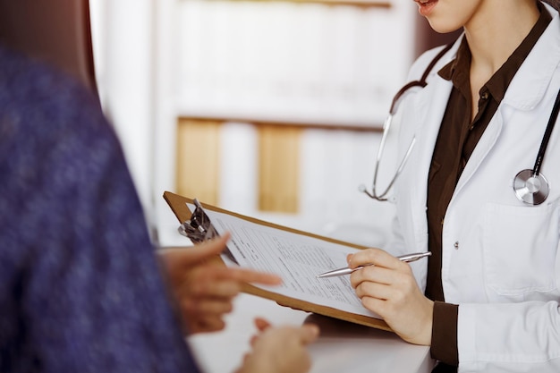 Médico e paciente discutindo o exame de saúde atual enquanto está sentado na clínica ensolarada. Serviço médico perfeito no hospital.