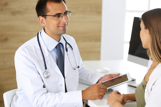 Médico e paciente discutindo resultados de exames médicos enquanto está sentado na mesa na clínica