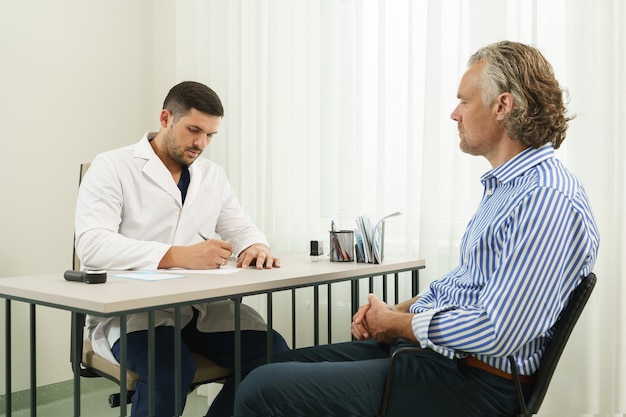 Médico e paciente do sexo masculino de meia idade durante a consulta no escritório