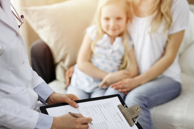 Médico e paciente. Pediatra usando a área de transferência enquanto examina a garotinha com a mãe em casa. Feliz criança caucasiana bonita no exame médico. Conceito de medicina.