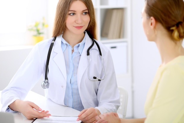 Médico e paciente sentados na mesa perto da janela, o sol brilha