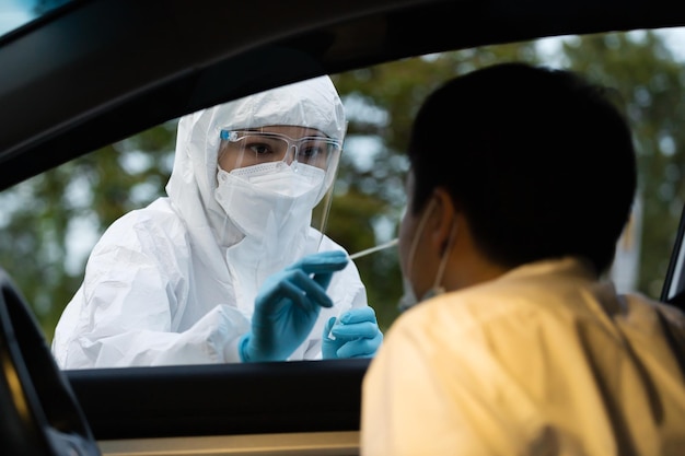 Médico em coronavírus de teste de traje de ppe (covid-19) para homem no carro por cotonete nasal, teste rápido de drive thru