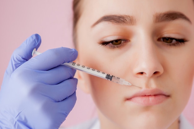 Médico em luvas dando injeções de botox em mulheres nos lábios, no espaço rosa