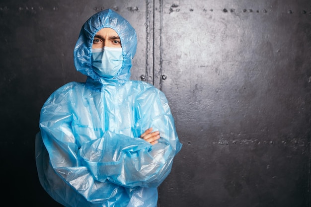 Médico em pé com as mãos cruzadas, usando roupa de proteção e máscara facial