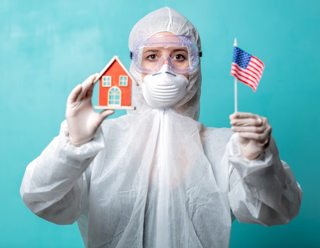 Médico em roupas de proteção possui bandeira dos EUA e casa de brinquedo