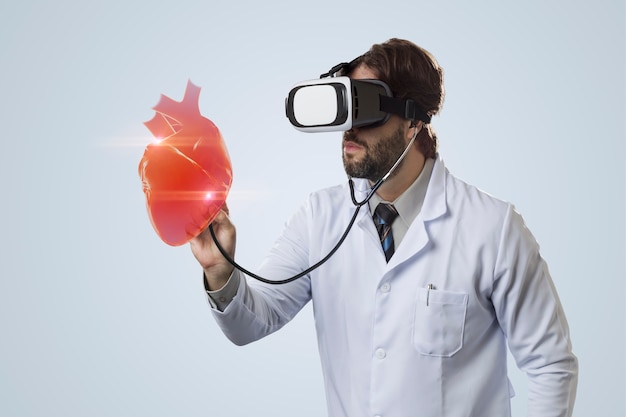 Médico em um fundo cinza usando óculos de realidade virtual, olhando para um coração virtual.