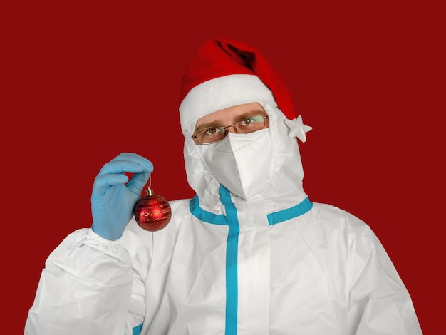 médico em um traje antiviral protetor e chapéu de Papai Noel segurando um balão de Natal