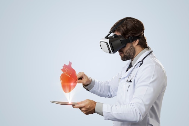 Médico em uma parede cinza usando óculos de realidade virtual, olhando para um coração virtual