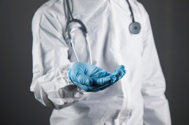 Médico em uniforme de proteção mostra as palmas das mãos abertas. mãos em forma de suporte em uma cena cinza