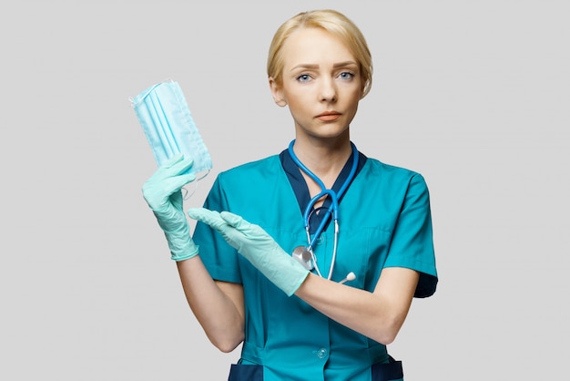 Médico enfermeira mulher com estetoscópio sobre parede cinza clara - mostrando a máscara protetora
