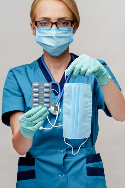 Médico enfermeira mulher vestindo máscara protetora e luvas de borracha ou látex - segurando bolhas de comprimidos