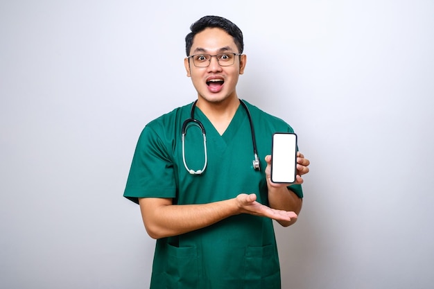 Médico enfermeiro jovem asiático vestindo uniforme e estetoscópio olhando para a câmera mostrando a tela do smartphone em branco recomendando o aplicativo