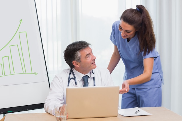 Médico y enfermera discutiendo algo en la computadora portátil durante la reunión