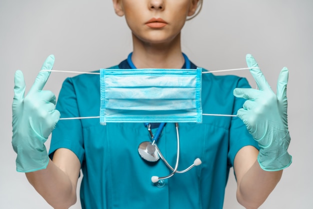Médico enfermera mujer con estetoscopio sobre pared gris claro - mostrando máscara protectora