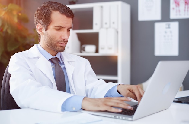 Médico enfocado sentado en su escritorio usando su portátil