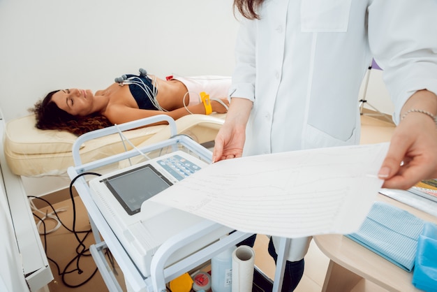 Médico con equipo de electrocardiograma haciendo prueba de cardiograma al paciente en la clínica.