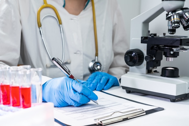 El médico escribe los resultados de un análisis de sangre en un formulario. Lugar de trabajo del médico: microscopio, tubos de ensayo con sangre.