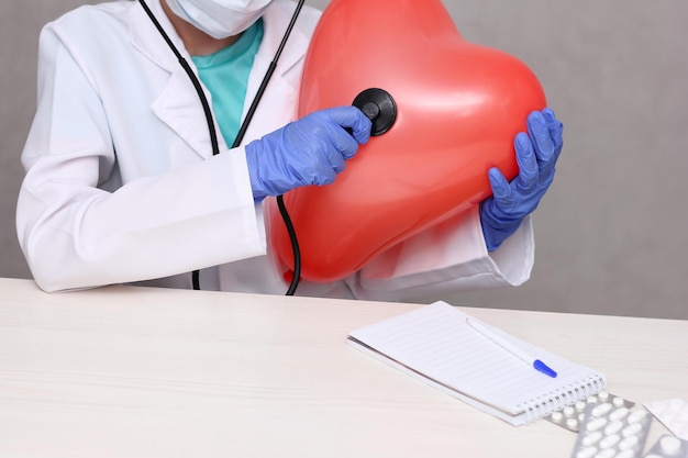 Un médico escuchando un gran corazón inflable con un estetoscopio Idea de cardiología y enfermedades del corazón