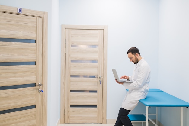 Médico especialista en el corredor de su clínica con su laptop