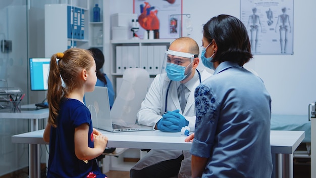 Médico especialista examinando raio-x infantil no hospital durante a pandemia. Médico pediatra com máscara de proteção prestando serviços de saúde, consulta, tratamento radiográfico em consultório médico.