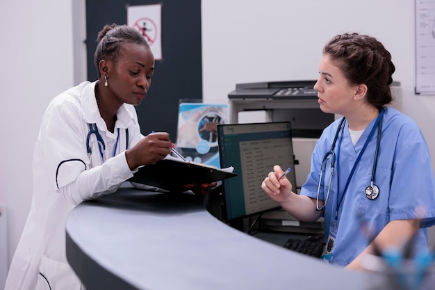 Médico especialista mostrando relatório médico ao assistente discutindo os sintomas do paciente trabalhando no tratamento medicamentoso na sala de espera do hospital. O médico está consultando outros profissionais de saúde
