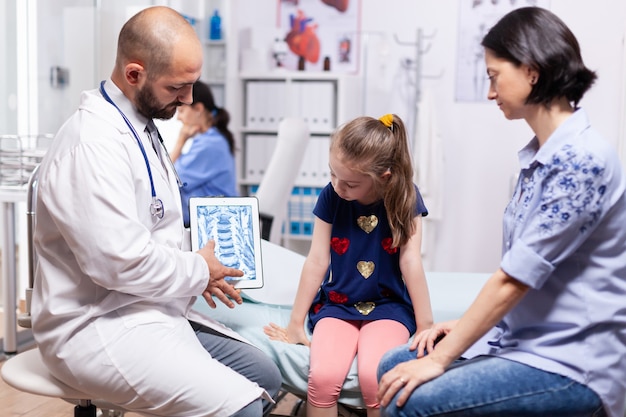 Foto médico especialista, segurando o tablet com radiografia durante o exame médico da criança no consultório do hospital. pediatra explicando tratamento de doenças, prestando serviços de saúde