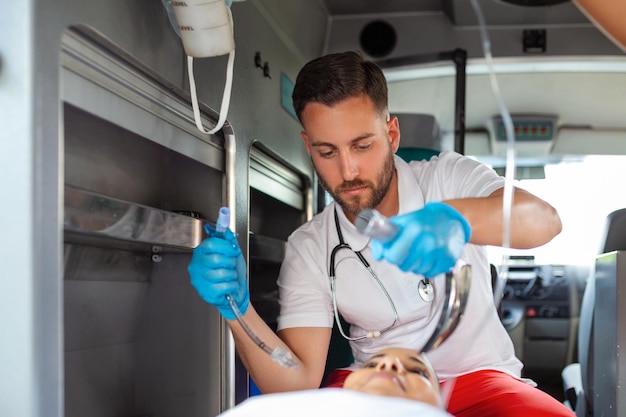 Médico está pronto para intubação endotraqueal para paciente que não respira Jovem paramédica segurando solução intravenosa Paramédicos do EMS fornecem ajuda médica a um paciente ferido a caminho de um hospital