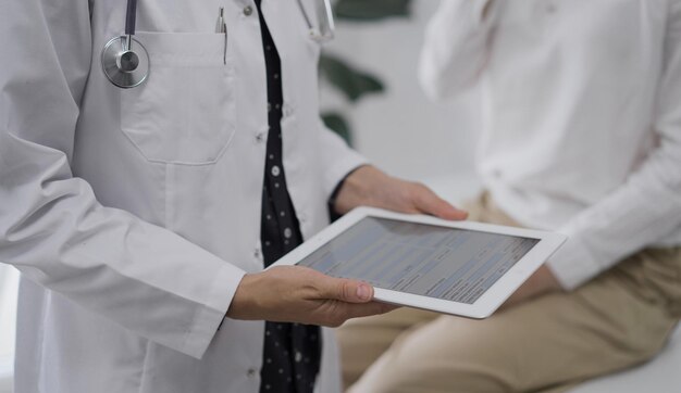 El médico está usando una tableta junto a una mujer joven durante una consulta en la clínica.