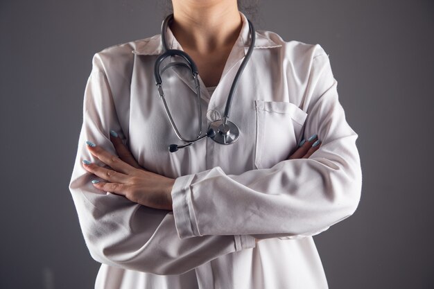 Un médico con un estetascopio se encuentra con las manos cruzadas sobre un fondo gris