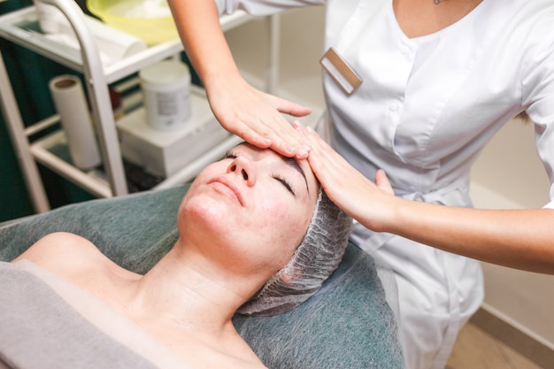 Médico esteticista faz massagem facial cosmética. A mulher relaxa em uma cadeira cosmética