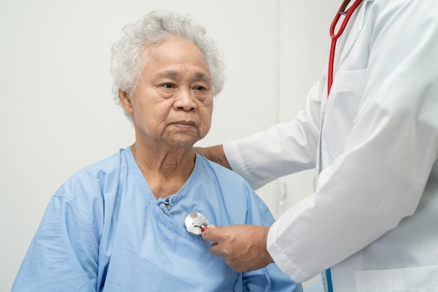 Médico con estetoscopio revisando a una anciana mayor o anciana mientras está sentada en una cama en la sala del hospital de enfermería concepto médico fuerte y saludable