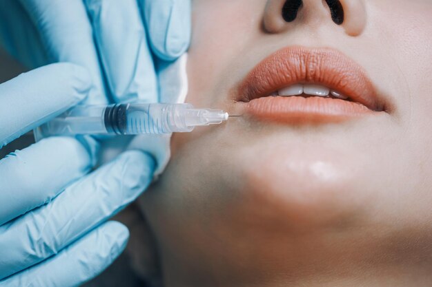El médico del estudio de belleza realiza inyecciones cosméticas en la piel de la cara de un paciente joven.