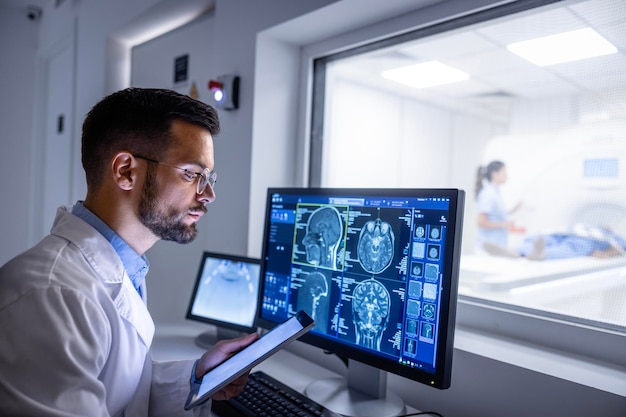 El médico examina las imágenes de rayos X en exhibición en la sala de control de RMN