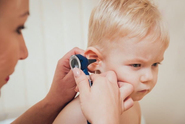 El médico examina el oído con otoscopio en una sala de pediatría.