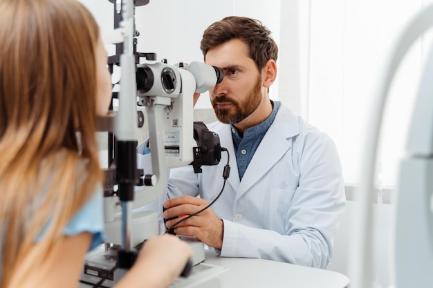 Médico examinando los ojos de una niña con equipo oftalmológico en una clínica moderna Concepto de atención médica