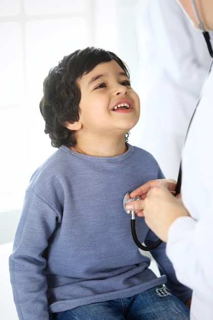 Foto médico examinando a un paciente infantil con estetoscopio lindo niño árabe en cita médica concepto de medicina y atención médica