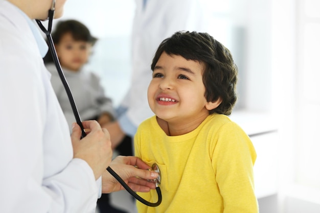 Foto médico examinando a un paciente infantil con estetoscopio lindo niño árabe en cita médica concepto de medicina y atención médica