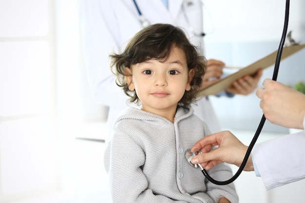 Foto médico examinando a un paciente infantil con estetoscopio lindo niño árabe en cita médica concepto de medicina y atención médica