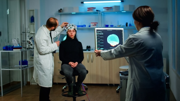 Foto médico examinando sensores de fone de ouvido eeg, monitorando funções cerebrais, enquanto pesquisador médico analisando tomografia no monitor, trabalhando em laboratório neurológico científico