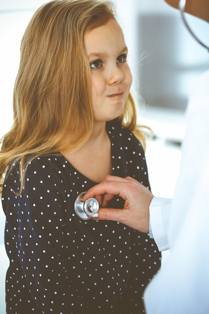 Médico examinando um paciente infantil pelo estetoscópio. Menina bonita na consulta médica. Conceito de medicina. Foto tonificada