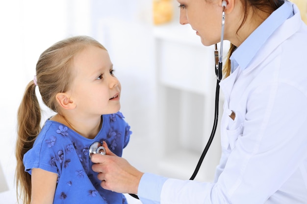 Médico examinando uma garotinha pelo estetoscópio. Paciente criança sorridente feliz na inspeção médica habitual. Conceitos de medicina e saúde.