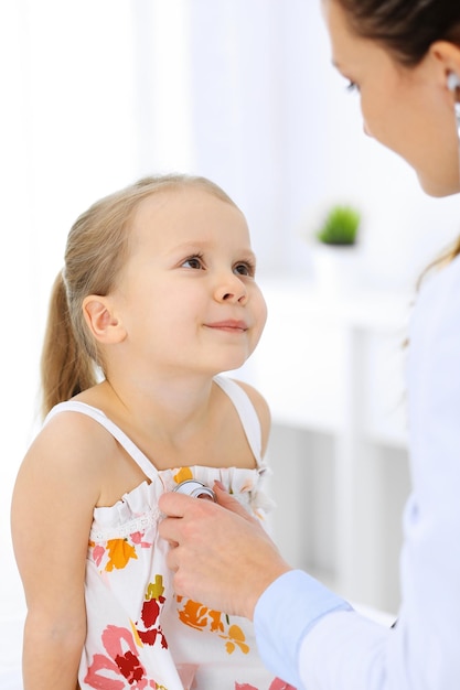 Médico examinando uma garotinha pelo estetoscópio. Paciente criança sorridente feliz na inspeção médica habitual. Conceitos de medicina e saúde.