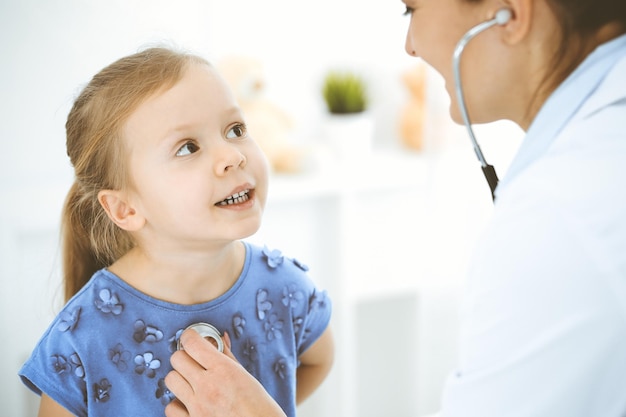 Médico examinando uma garotinha pelo estetoscópio. Paciente criança sorridente feliz na inspeção médica habitual. Conceitos de medicina e saúde.