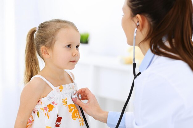 Médico examinando uma garotinha pelo estetoscópio. Paciente criança sorridente feliz na inspeção médica habitual. Conceitos de medicina e saúde.