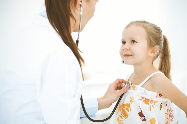 Médico examinando uma garotinha pelo estetoscópio Paciente criança sorridente feliz na inspeção médica habitual Conceitos de medicina e saúde