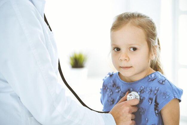 Médico examinando uma garotinha pelo estetoscópio Paciente criança sorridente feliz na inspeção médica habitual Conceitos de medicina e saúde