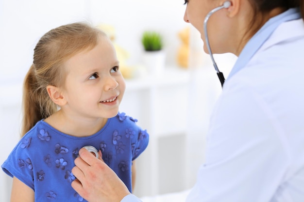 Médico examinando uma garotinha pelo estetoscópio. Paciente criança sorridente feliz na inspeção médica habitual. Conceitos de medicina e saúde.