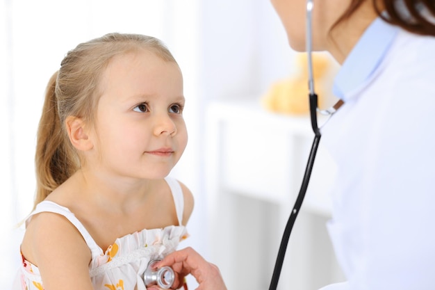 Médico examinando uma garotinha pelo estetoscópio. Paciente criança sorridente feliz na inspeção médica habitual. Conceitos de medicina e saúde.